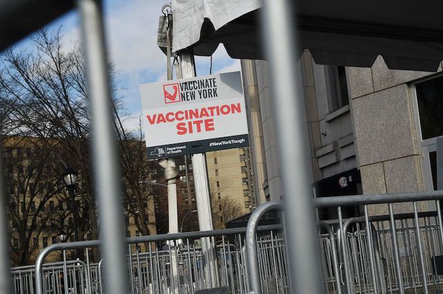 A white sign that says Vaccinate New York outside the Yankee Stadium megasite in the Bronx next to metal barricades.